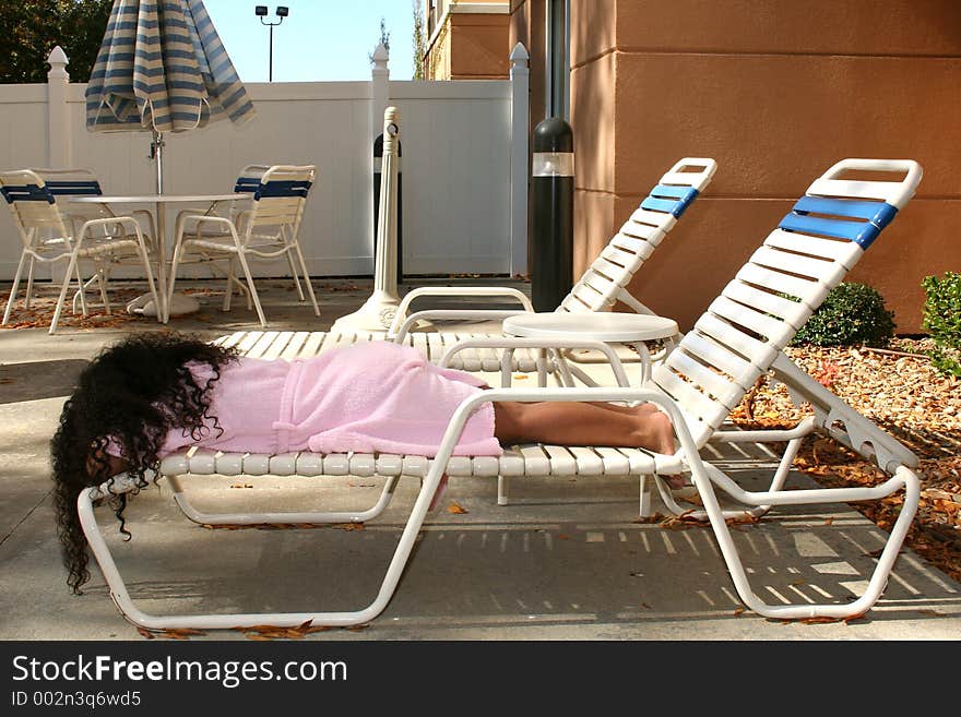 Seven year old girl asleep outside in lounge chair wearing pink pool robe. Seven year old girl asleep outside in lounge chair wearing pink pool robe.