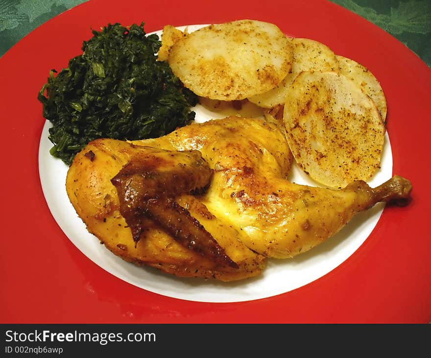 Photo of cornish game hen, potatos and spinach served on a red Christmas plate.