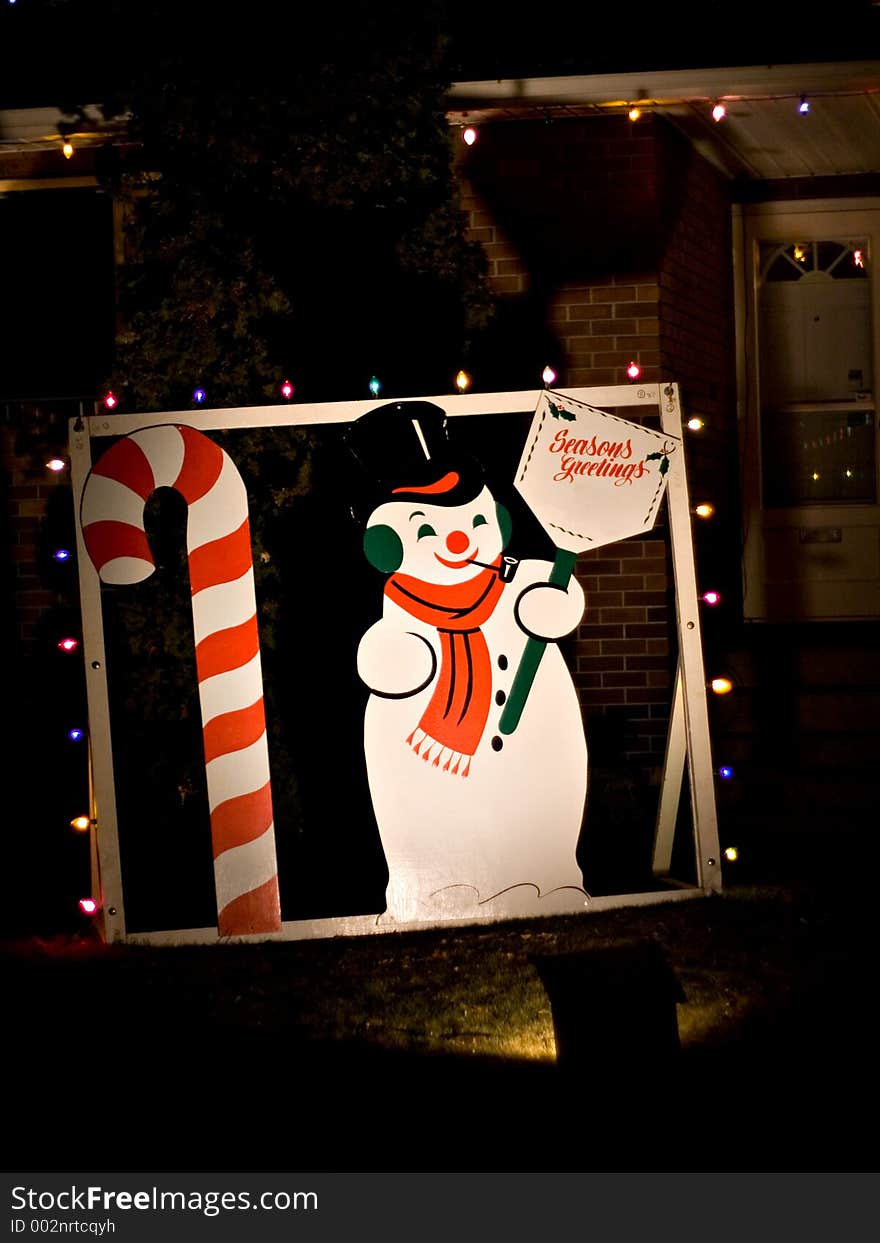 A snowman and candy cane decorate the front lawn of a home during the holiday season.