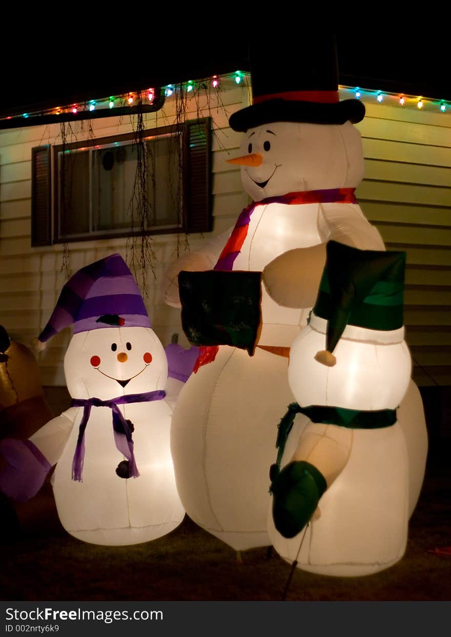 Thre snowmen decorate the front lawn of a home during the holiday season. Thre snowmen decorate the front lawn of a home during the holiday season.