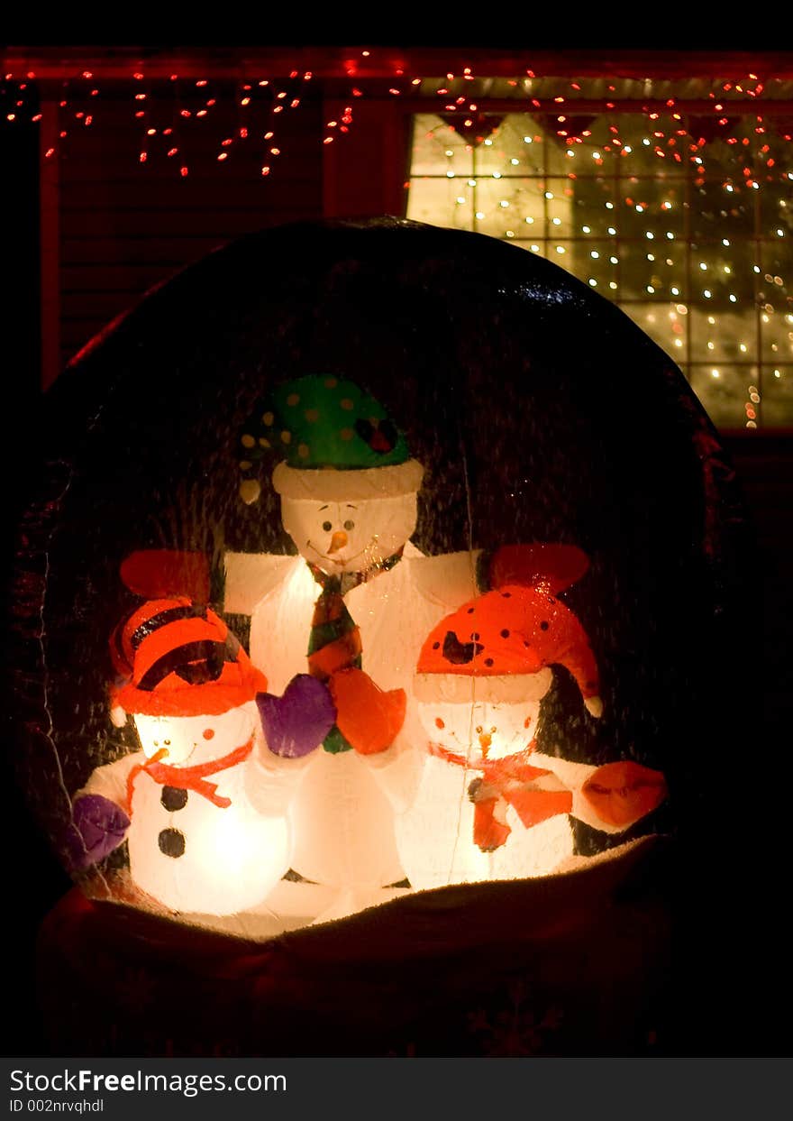 Three snowmen in a glass globe adorn a front lawn at Christmas. Three snowmen in a glass globe adorn a front lawn at Christmas.