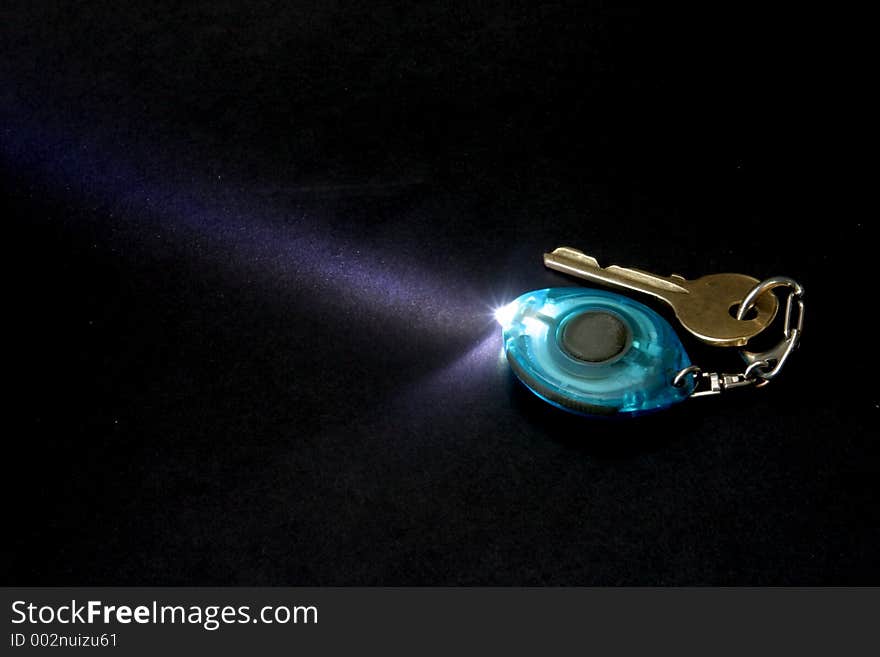 Key ring flashlight with door key - isolated on black. Key ring flashlight with door key - isolated on black