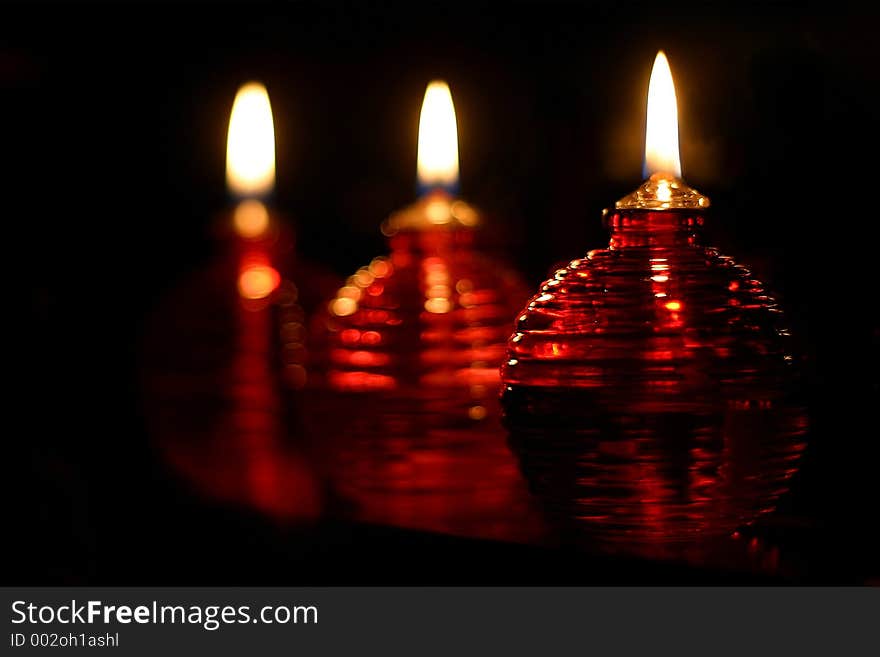 Three red oil lamps standing on a shelf. Focus is on the one in front.