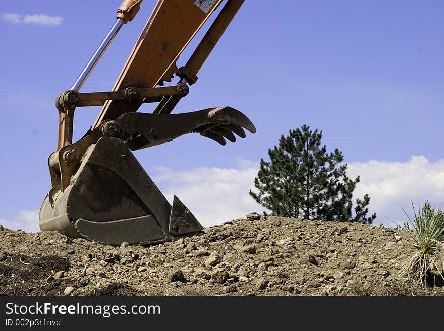 The claws of a steamshovel attempt to scoop up a tree on a bright blue sky day. The claws of a steamshovel attempt to scoop up a tree on a bright blue sky day.