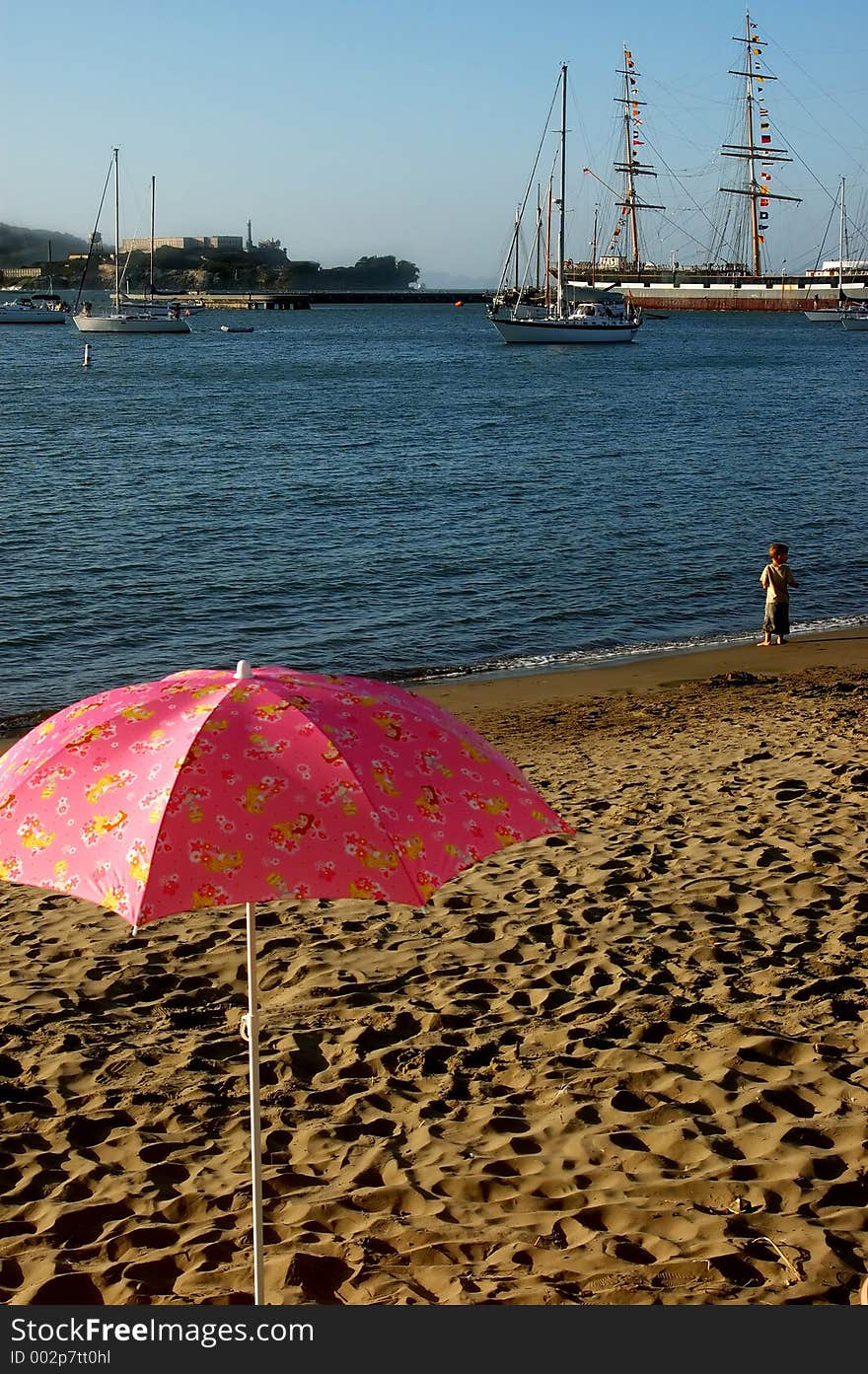 Pink umbrella in sand on beach in San Francisco, CA.