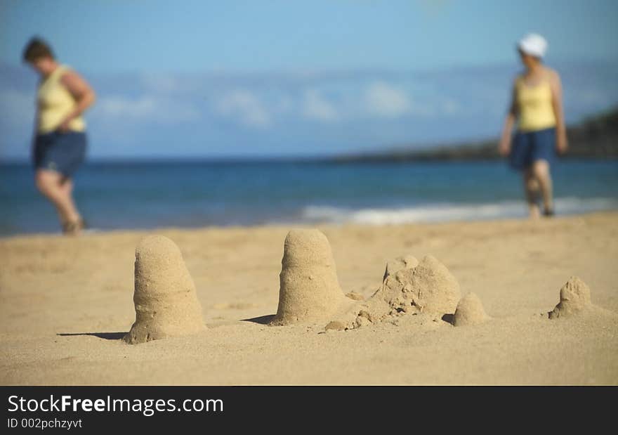 Two women walking behind sand castles. Two women walking behind sand castles