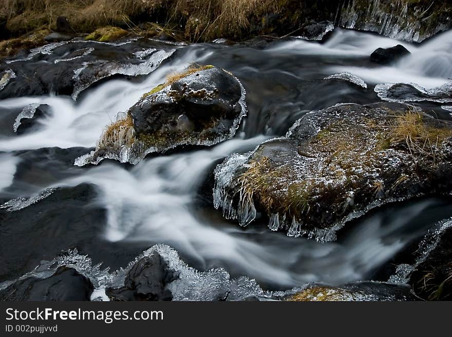 Water running around frozen stones in a stream. Water running around frozen stones in a stream