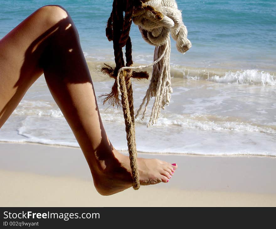 Attractive woman's leg sways in a rope swing in the most beautiful beach in the world. Attractive woman's leg sways in a rope swing in the most beautiful beach in the world.