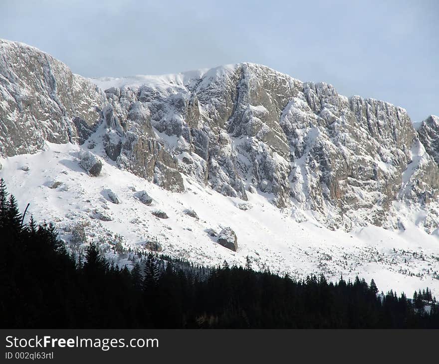 Mountain Peaks Covered With Snow And Little Forest Downhill