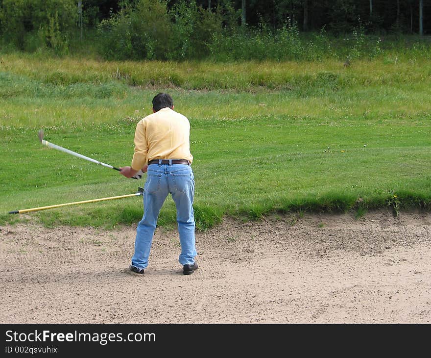 A man makes a shot from a sand trap. A man makes a shot from a sand trap.