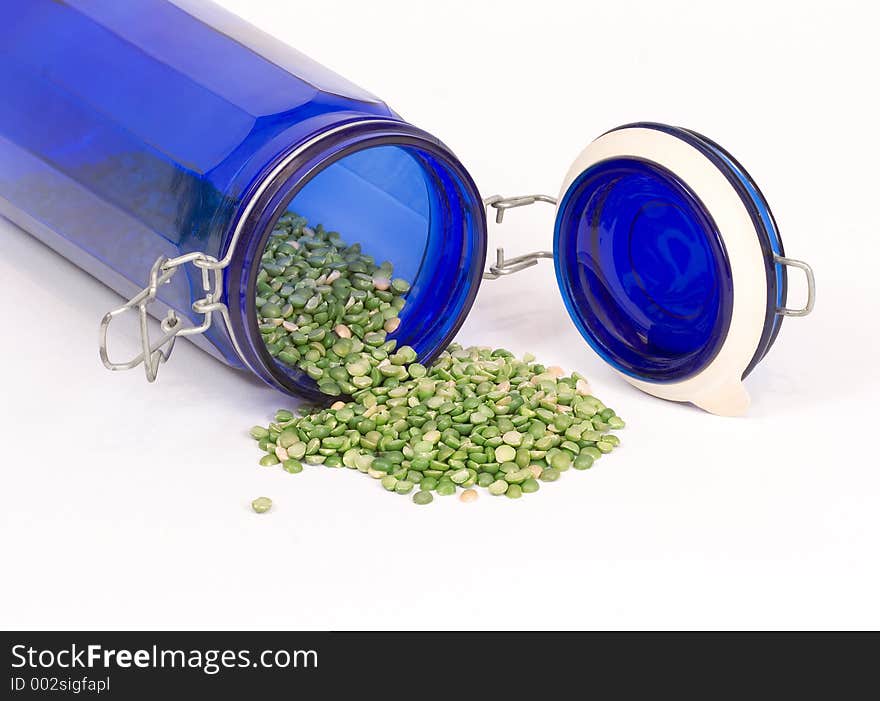 Dried split peas spilling out of a blue glass canister onto a white linen cloth. Dried split peas spilling out of a blue glass canister onto a white linen cloth