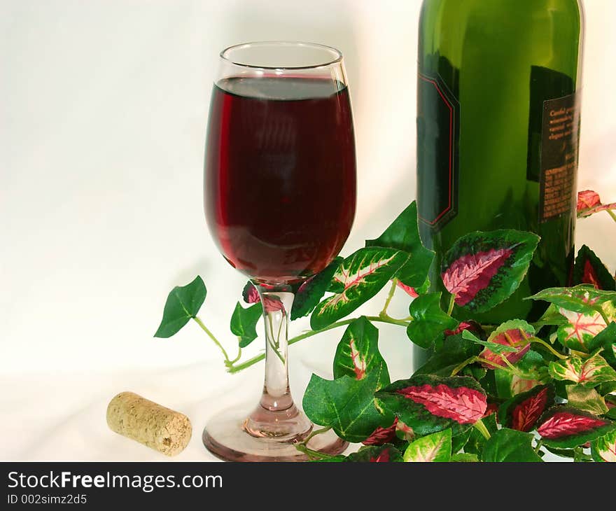 Solo glass of red wine and wine bottle amongst ivy leaves.