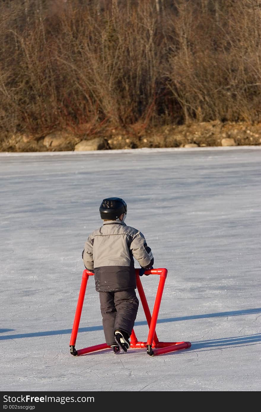 A young boy takes a leisurely skate while leaning on a learning tool for support. A young boy takes a leisurely skate while leaning on a learning tool for support.