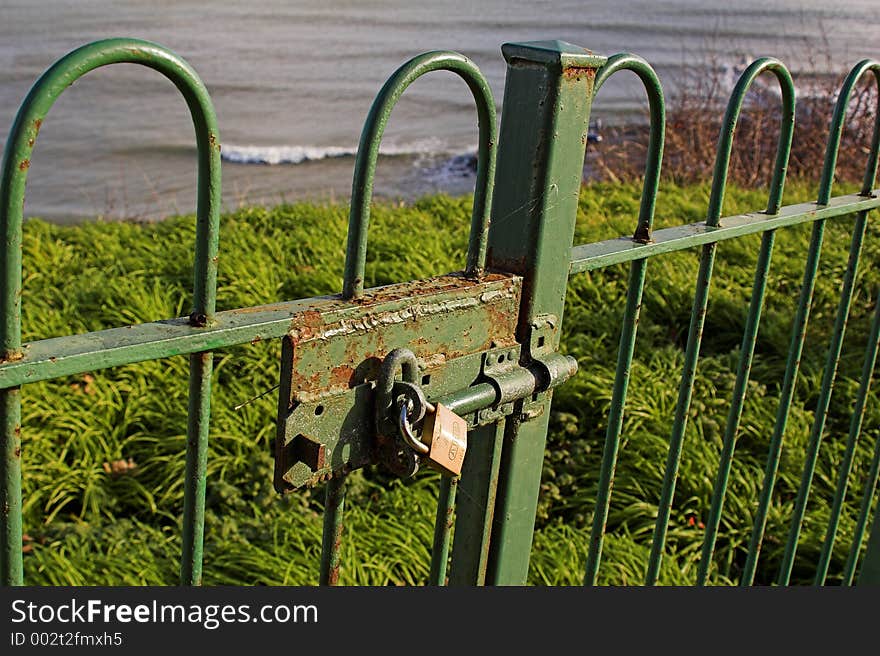 Padlock on green gate overlooking grass and sea. Padlock on green gate overlooking grass and sea.