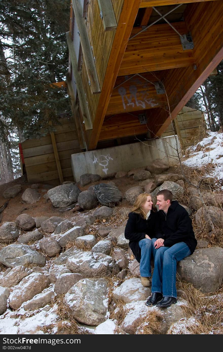 A young couple shares a happy moment together while seated under a bridge in winter. A young couple shares a happy moment together while seated under a bridge in winter.