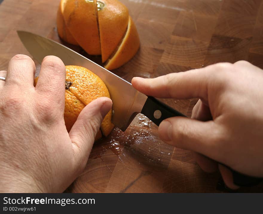 Hands slicing oranges on wooden cutting board. Hands slicing oranges on wooden cutting board