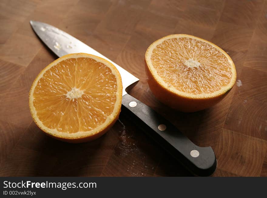 Orange sliced in half with knife on wooden cutting board. Orange sliced in half with knife on wooden cutting board