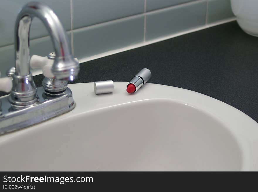 A rosy red lipstick rests on a white sink in a retro bathroom, as if the lady applying it has been interrupted.