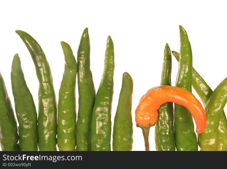 A wall of green chilis with one orange chili that is slightly bent. A wall of green chilis with one orange chili that is slightly bent