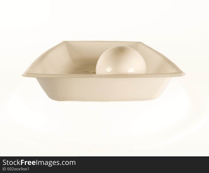 An isolated egg surrounded by a white background sits in a dish. After its shell is compromised, it will be ready to be served for breakfast. An isolated egg surrounded by a white background sits in a dish. After its shell is compromised, it will be ready to be served for breakfast.