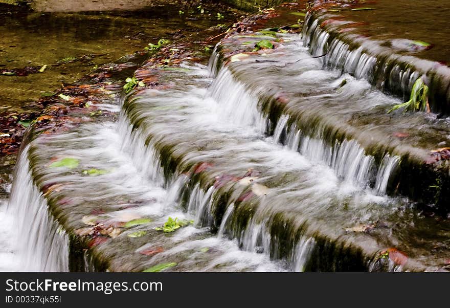 Manmade waterfall in park with autum leaves flowing in the water.