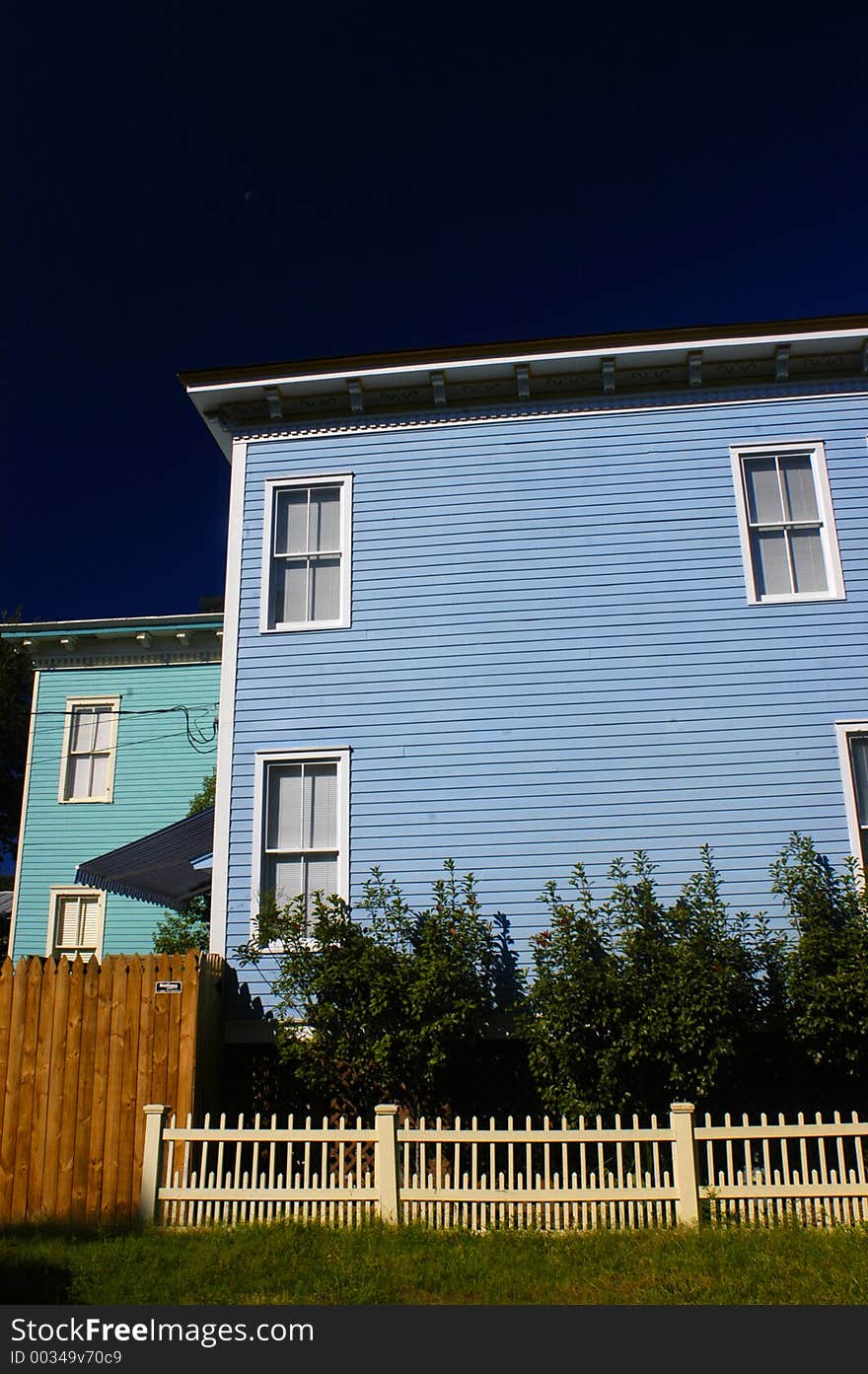 Blue and light blue boraded houses in front of deep blue sky with a white wicket fence infront. Blue and light blue boraded houses in front of deep blue sky with a white wicket fence infront.