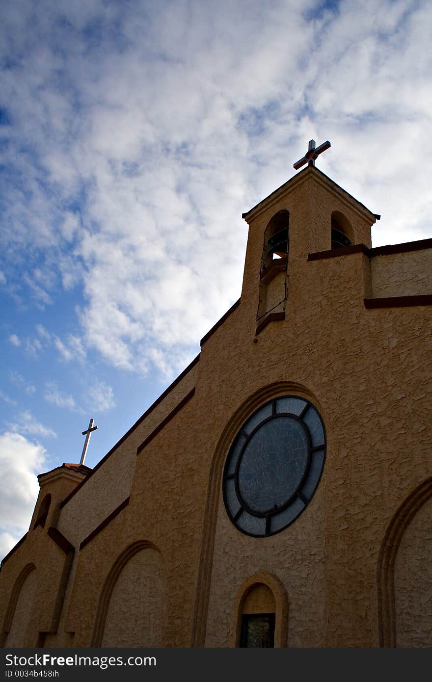 A vertical shot of a brick church against a sky decorated with cloud.