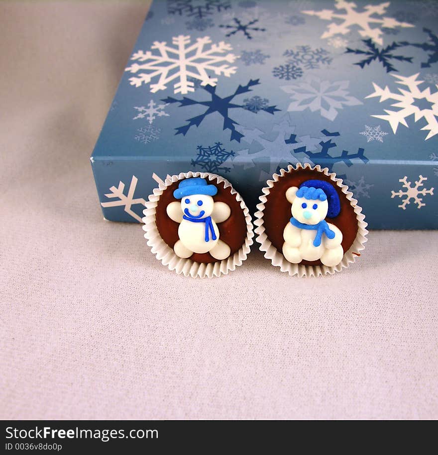 Snowman on chocolate against a box of chocolates, with snowflakes.