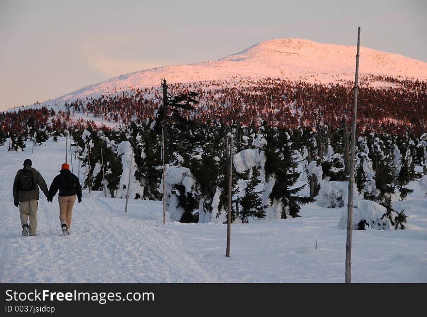 Young couple in love walking. A charming mountain lit by the sunset in the background. Young couple in love walking. A charming mountain lit by the sunset in the background.