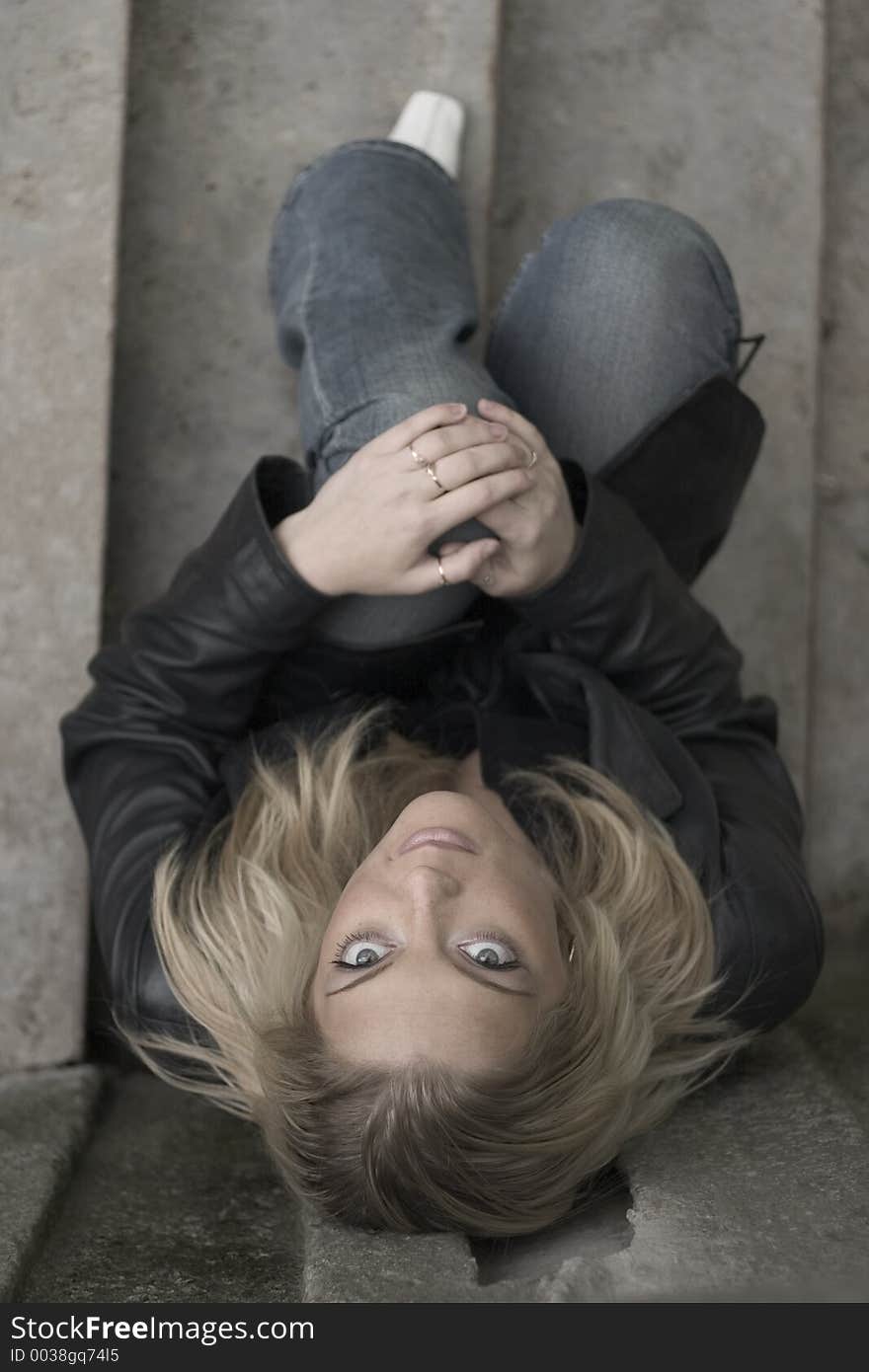 A young woman sitting on the steps, holding her knee, looking sad. A young woman sitting on the steps, holding her knee, looking sad