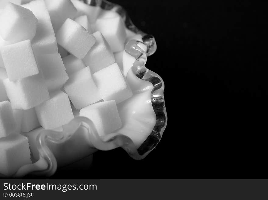 Macro of sugar cubes in frilly glass bowl against black. Macro of sugar cubes in frilly glass bowl against black