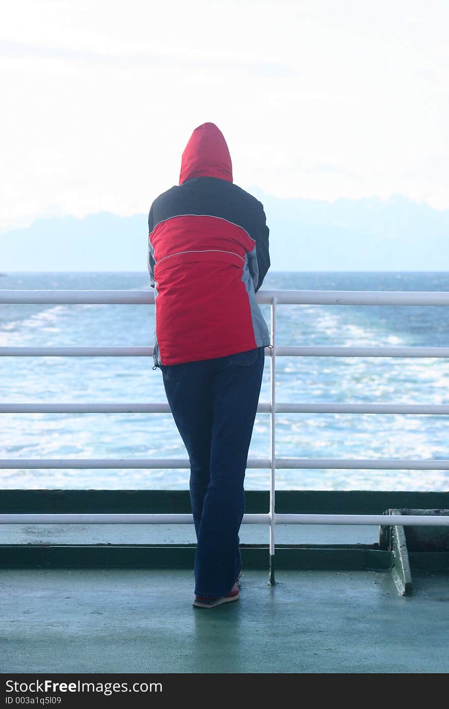 Alone man in the hood standing at the ferry and looking at the sea