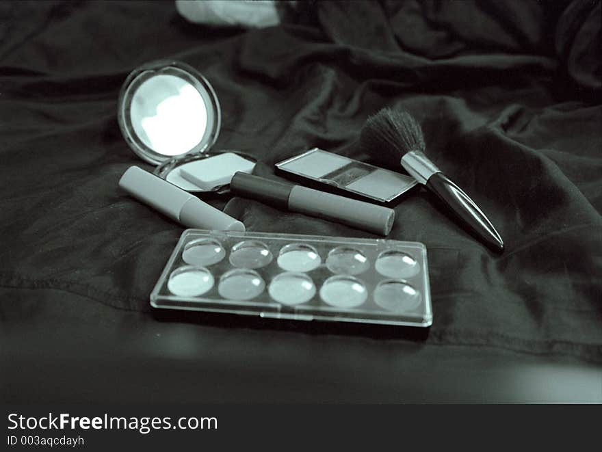 Various types of cosmetics positioned on a silk sheet, including blush, lipstick, and eyeliner. Various types of cosmetics positioned on a silk sheet, including blush, lipstick, and eyeliner.