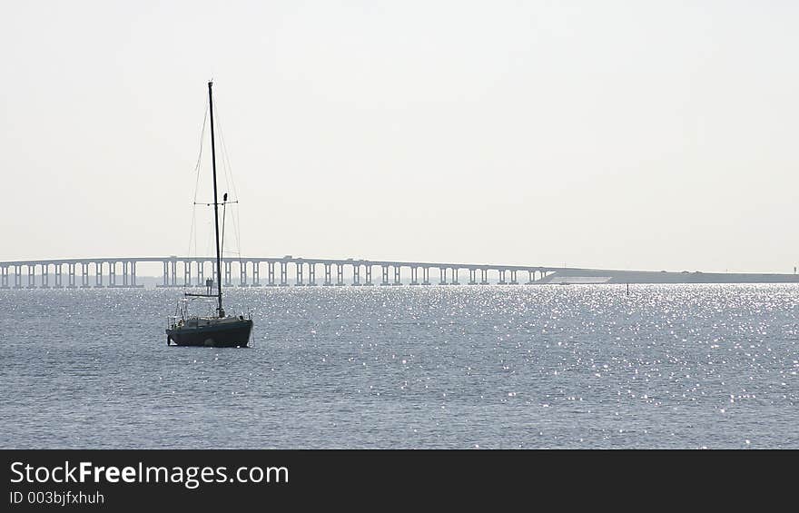 Sailboat at anchor in the Indian River, Rockledge, Florida. There's lots of sky and water and there's a bridge in the distance Photo ID: BeachScenes00001