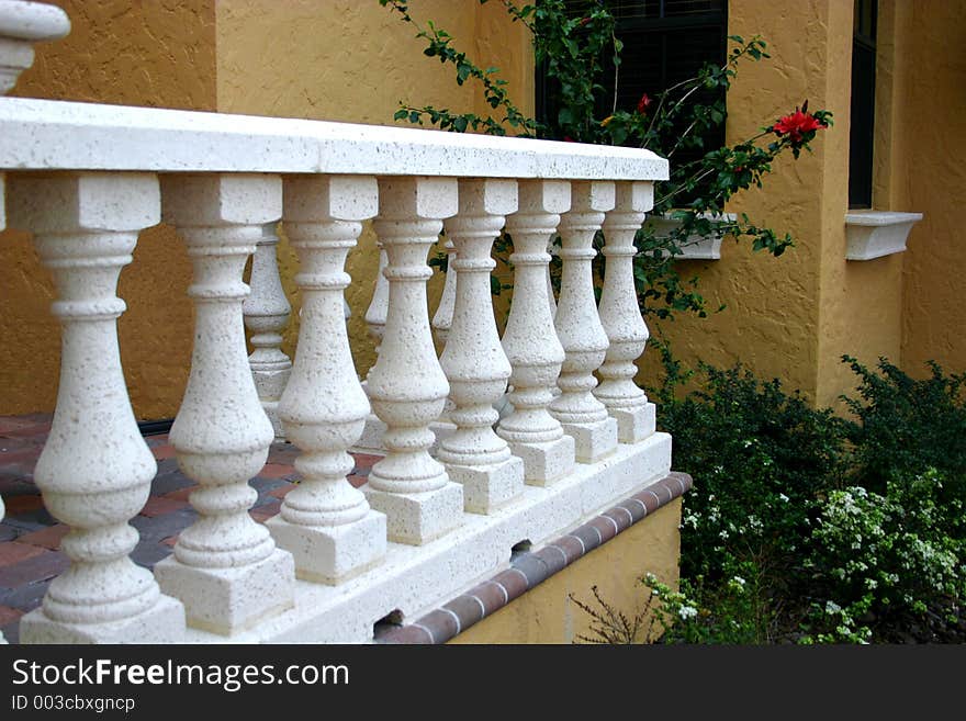 White columns and railing at entrance of home, with red flower peaking out. White columns and railing at entrance of home, with red flower peaking out