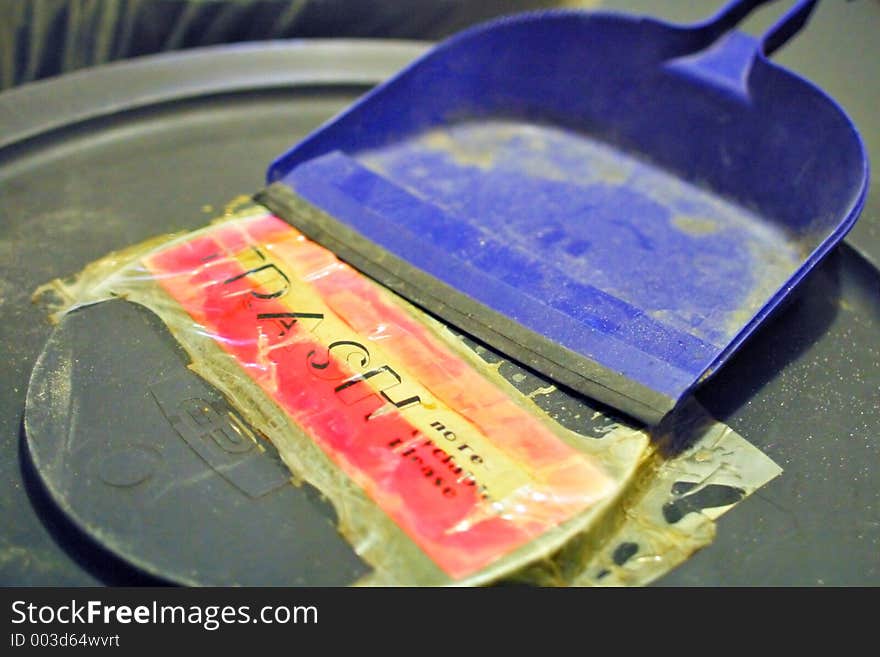 Blue dustpan on top of a trash can showing the word TRASH on a weathered sign. Blue dustpan on top of a trash can showing the word TRASH on a weathered sign.