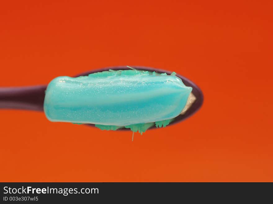 Toothbrush with toothpaste isolated on orange background shown from top. Toothbrush with toothpaste isolated on orange background shown from top