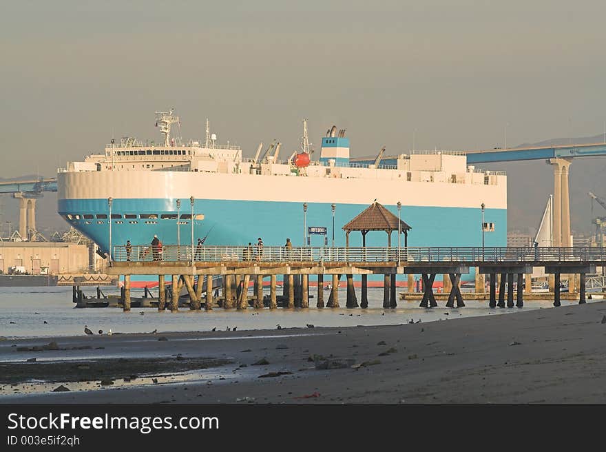 Cargo ship leaves Port of San Diego bound for Japan. Coronado ferry landing with young kids fishing in the midground.