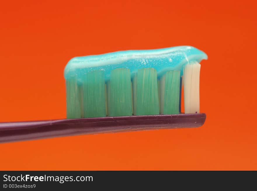 Macro of a toothbrush with toothpaste against orange background