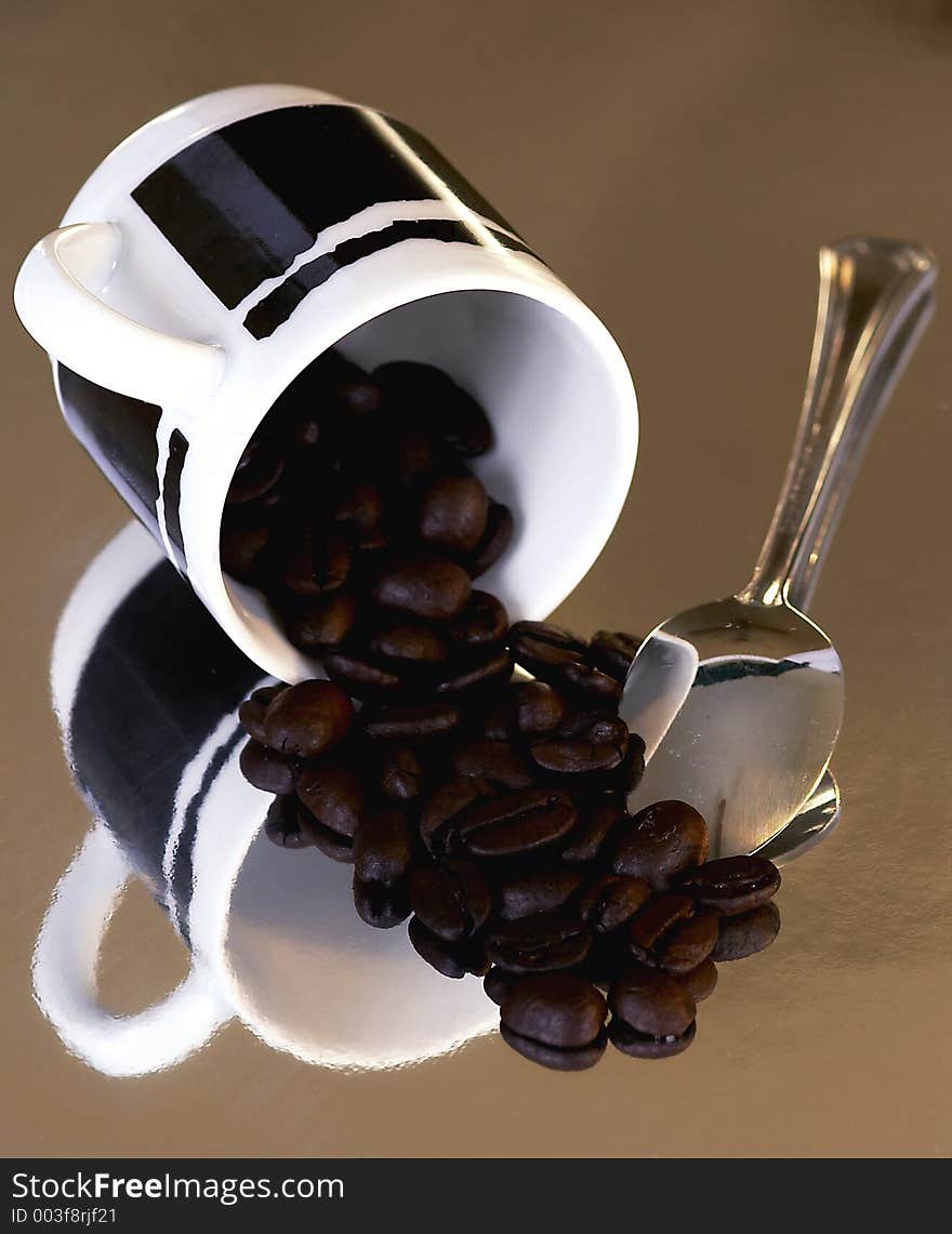 An espresso cup with roasted coffee beans and a small silver spoon. An espresso cup with roasted coffee beans and a small silver spoon