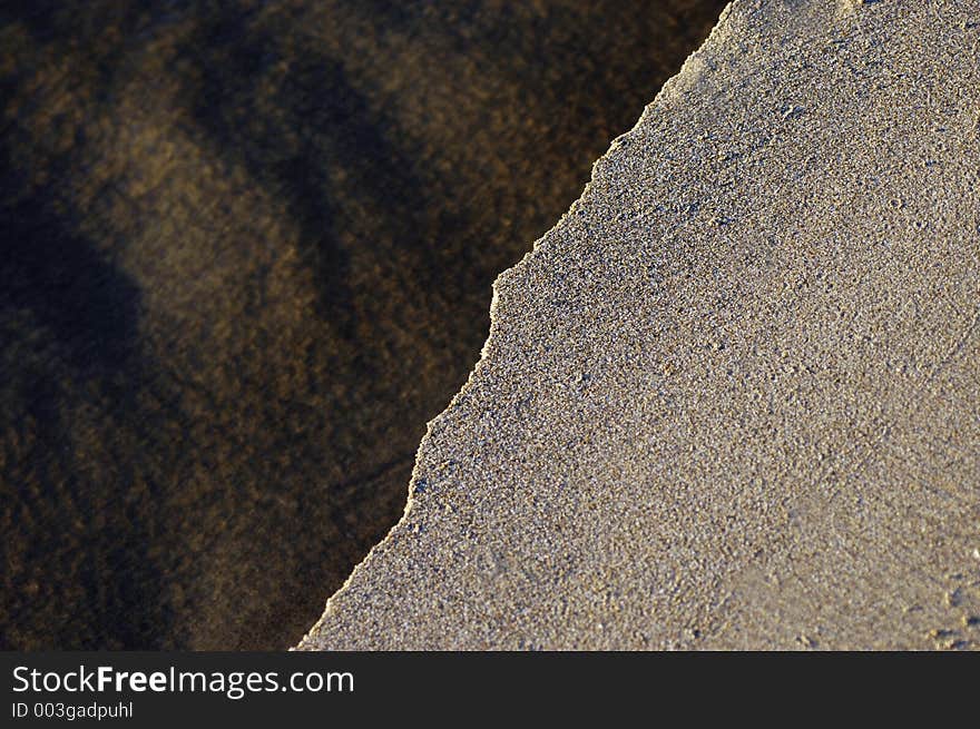 A small stream cuts through an area of flat sand in low sun. A small stream cuts through an area of flat sand in low sun