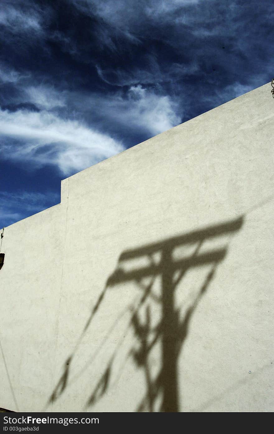 A utility pole casts a shadow on a concrete wall below a deep blue sky with wispy clouds. A utility pole casts a shadow on a concrete wall below a deep blue sky with wispy clouds