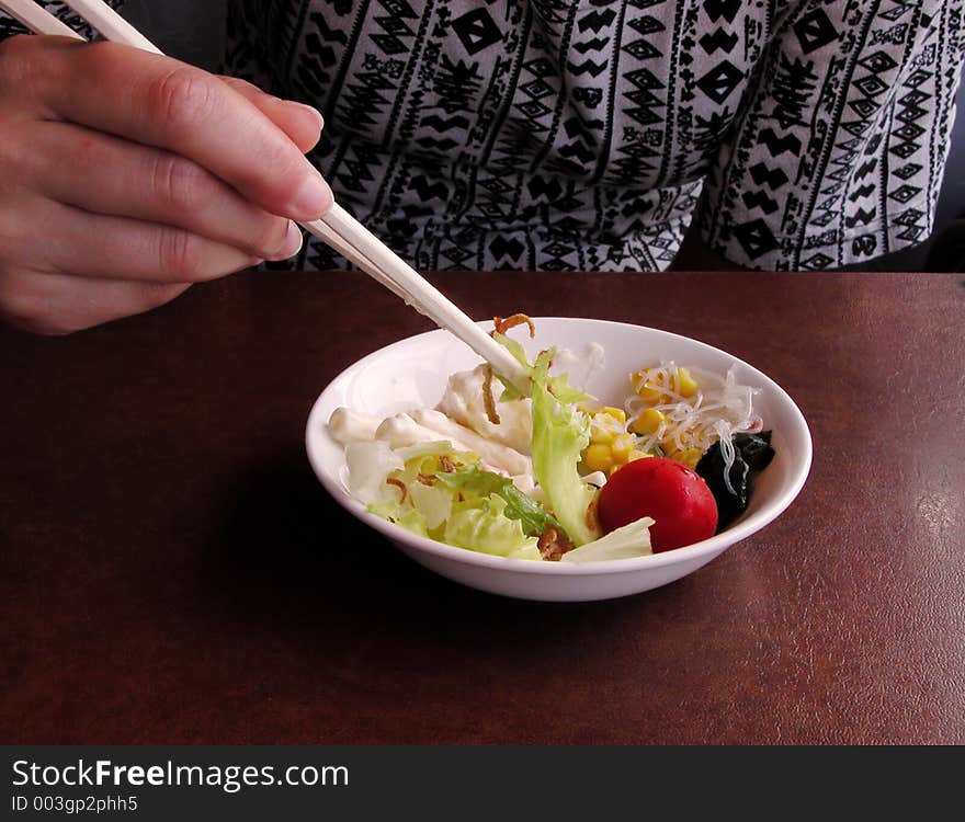 Girl eating salad with chopsticks at a restaurant table