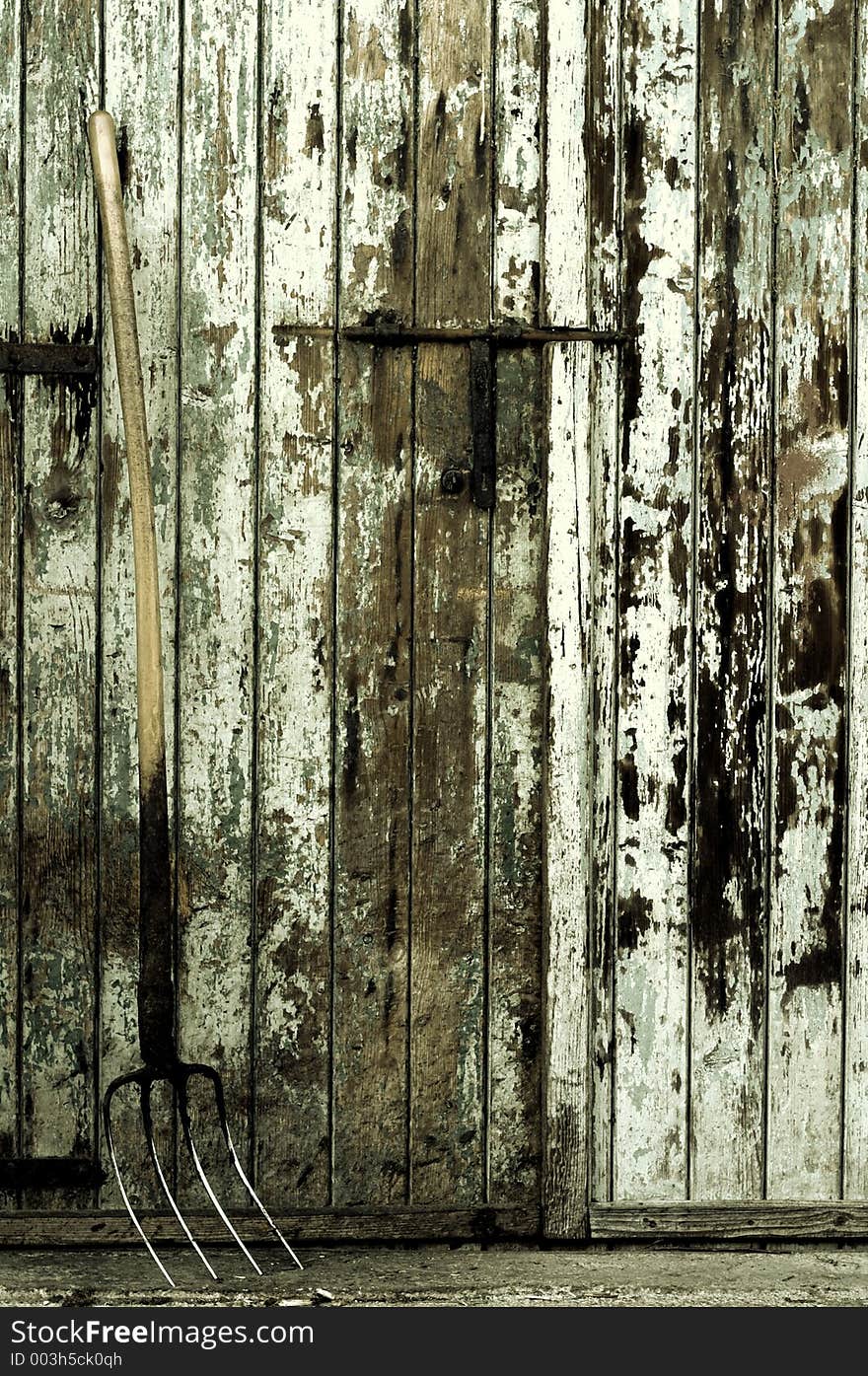 A fork tool in front of an old painted wooden farm door, toned. A fork tool in front of an old painted wooden farm door, toned.