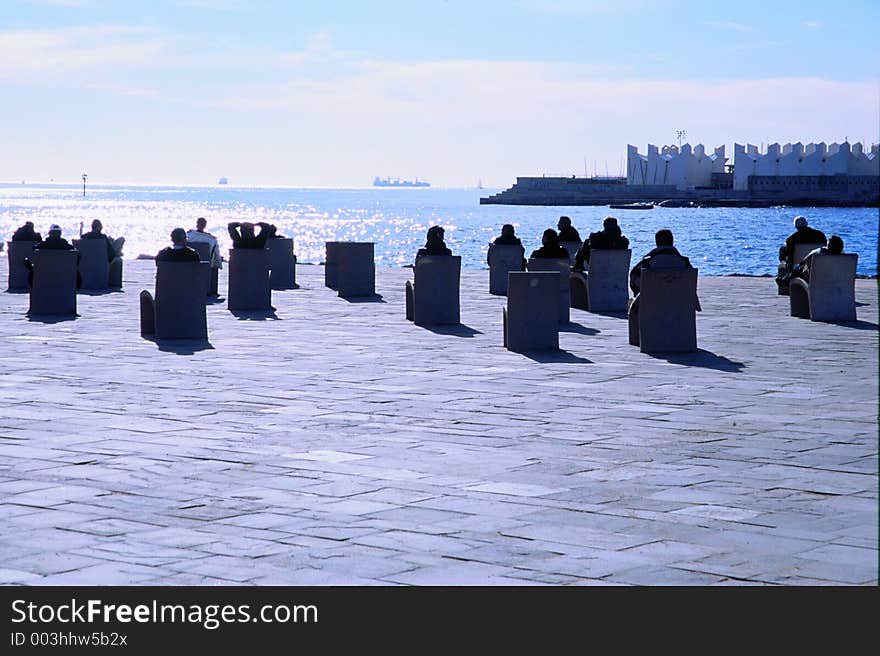 People relaxing on the waterfront on stone chairs. one could imagine that people were waiting for some kind of space ship to arrive for boarding. People relaxing on the waterfront on stone chairs. one could imagine that people were waiting for some kind of space ship to arrive for boarding