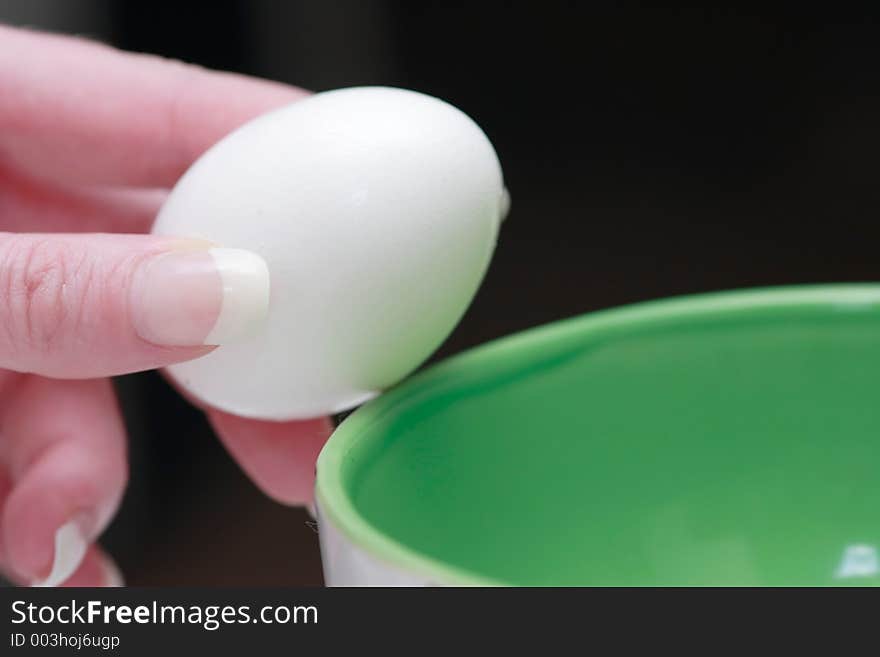 Hand holding an egg over green bowl