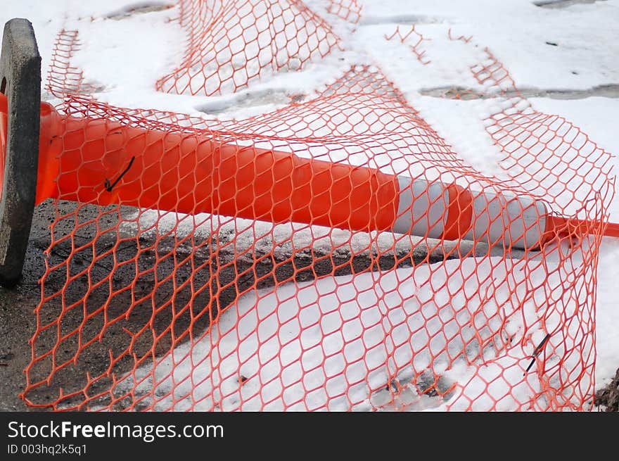 Orange construction cone tipped over with orange coated fencing ove it.