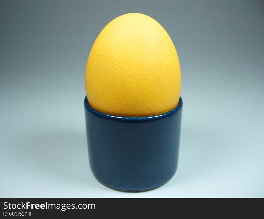 A yellow hen´s egg in a blue egg-cup. This could be part of the breakfast at Easter. A yellow hen´s egg in a blue egg-cup. This could be part of the breakfast at Easter.