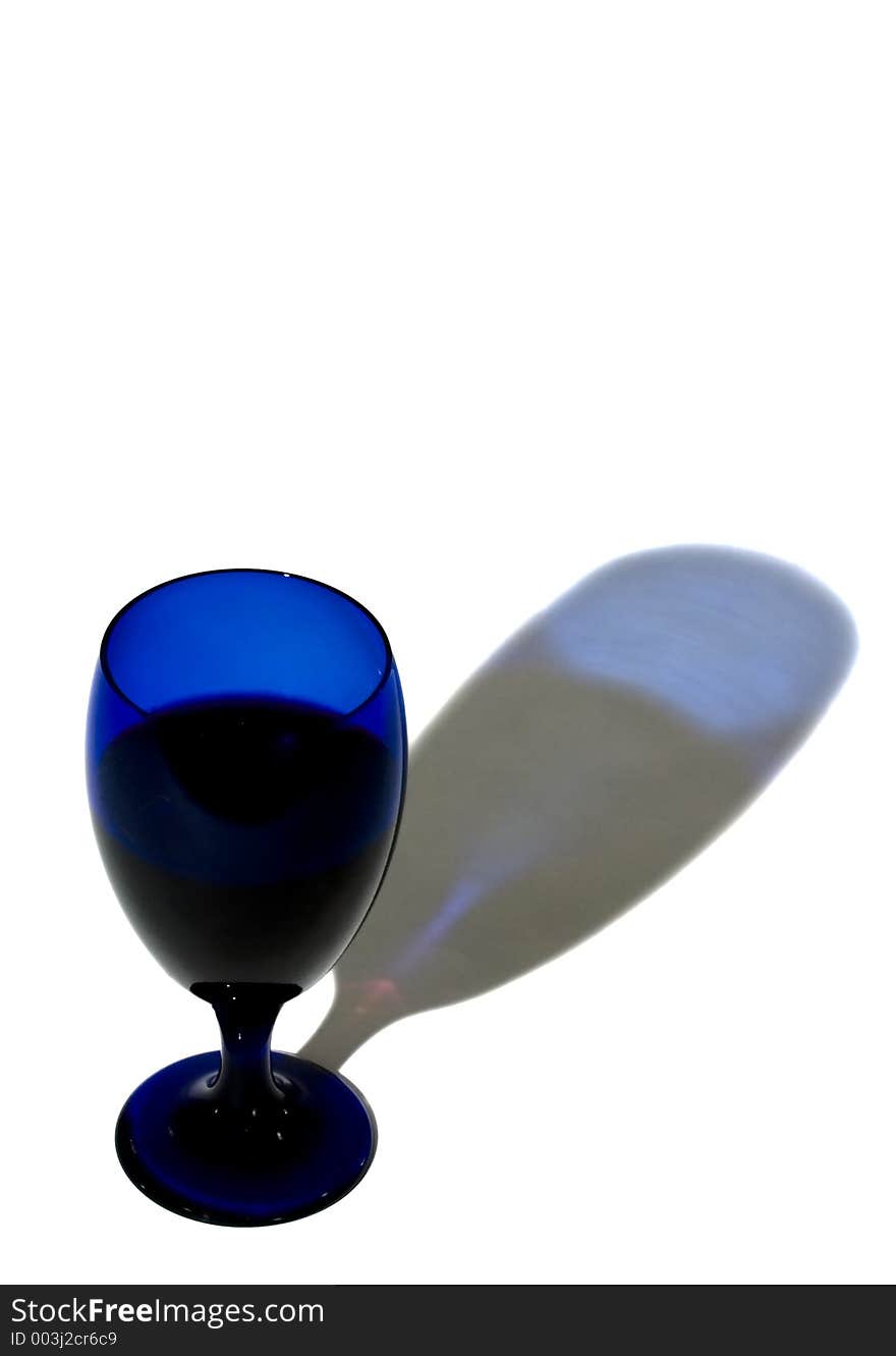 Cobalt blue glass filled with wine casts blue shadow on white background - copy space. Cobalt blue glass filled with wine casts blue shadow on white background - copy space