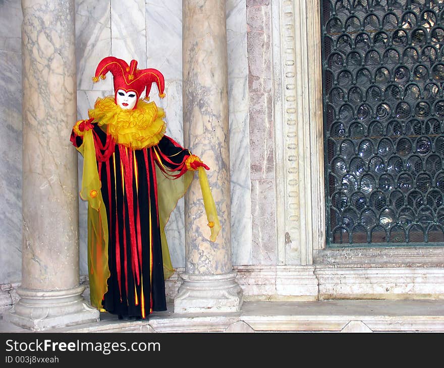 Carnival of Venice, Italy: Person wearing beautiful mask and costume in the colors red, yellow and black between two pillars made of marble. [[ More Carnival photos ]]. Carnival of Venice, Italy: Person wearing beautiful mask and costume in the colors red, yellow and black between two pillars made of marble. [[ More Carnival photos ]]